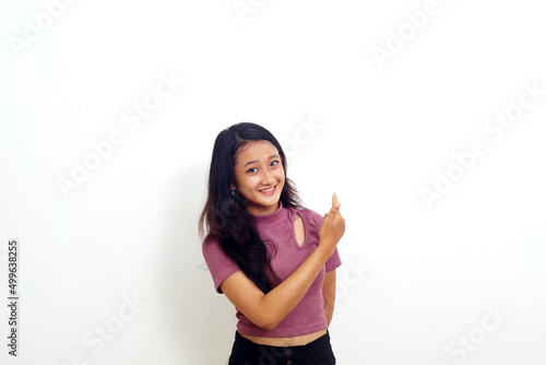Happy asian girl standing and pointing something at empty space. Isolated on white background