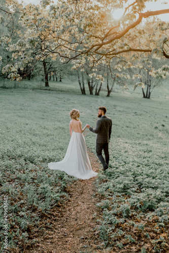 The bride and groom at sunset. The bride and groom walk along the path across the field.