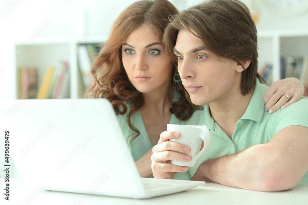 Portrait of happy young couple looking at laptop while drinking tea at home Portrait of happy young couple looking at laptop while drinking tea at home