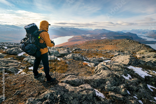 Male hiker overlooking epic view of vast arctic landscape of Stora Sjofallet National Park, Sweden, on autumn day. Mountains and valleys of Lapland. Ahkka massif. View from the top of Lulep Gierkav. photo