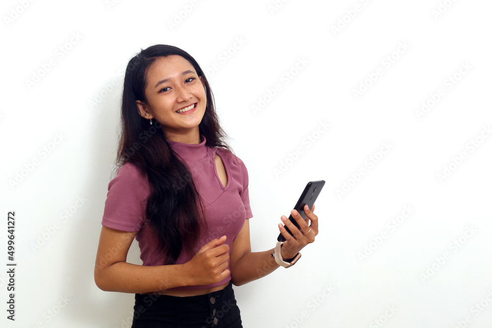 Smiling asian young girl standing while holding a cellular phone. Isolated on white Smiling asian young girl standing while holding a cellular phone. Isolated on white