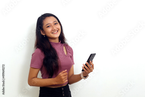 Smiling asian young girl standing while holding a cellular phone. Isolated on white