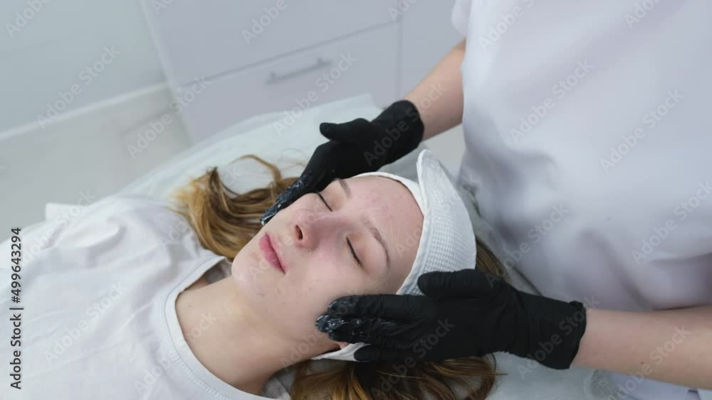 Cosmetologist applies a woman a therapeutic mask on her face. Woman in a spa salon on cosmetic procedures for facial care. Beautician makes a massage of the face with a moisturizing mask on a face. Cosmetologist applies a woman a therapeutic mask on her face. Woman in a spa salon on cosmetic procedures for facial care. Beautician makes a massage of the face with a moisturizing mask on a face.