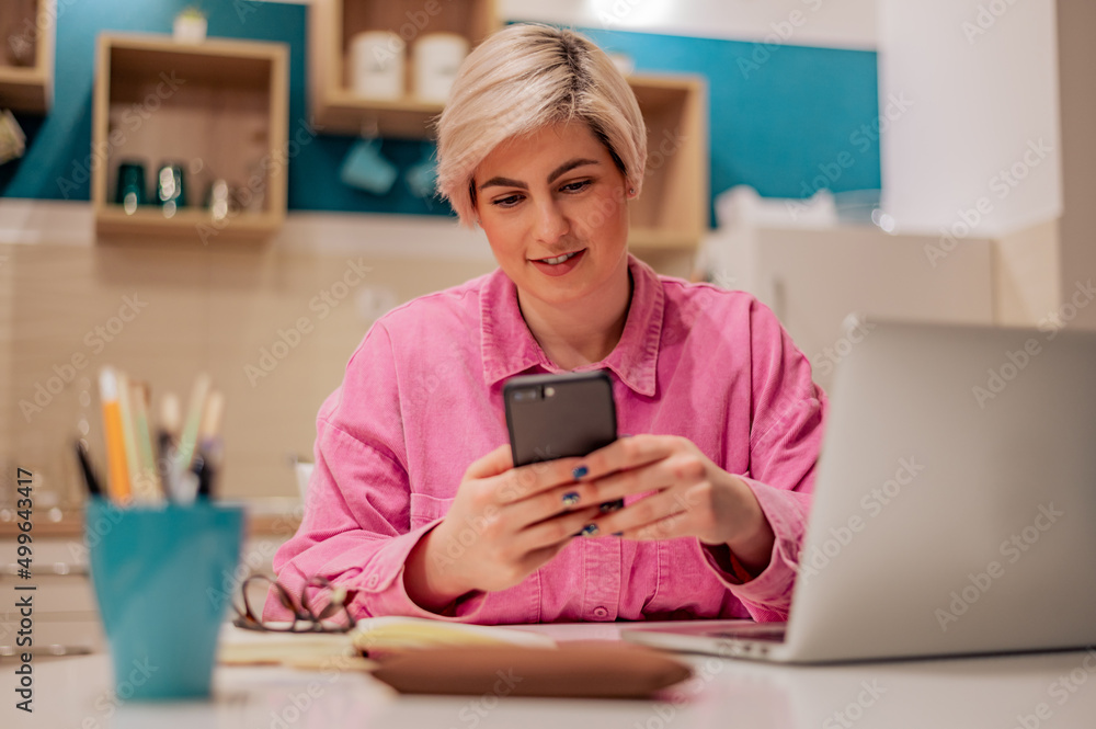 Woman with short hair using her smartphone and a modern laptop at home Woman with short hair using her smartphone and a modern laptop at home