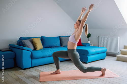 Woman training yoga at home an standing in warrior one pose.