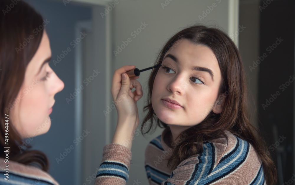 A young woman paints her eyelashes with mascara in front of a mirror. A young woman paints her eyelashes with mascara in front of a mirror.