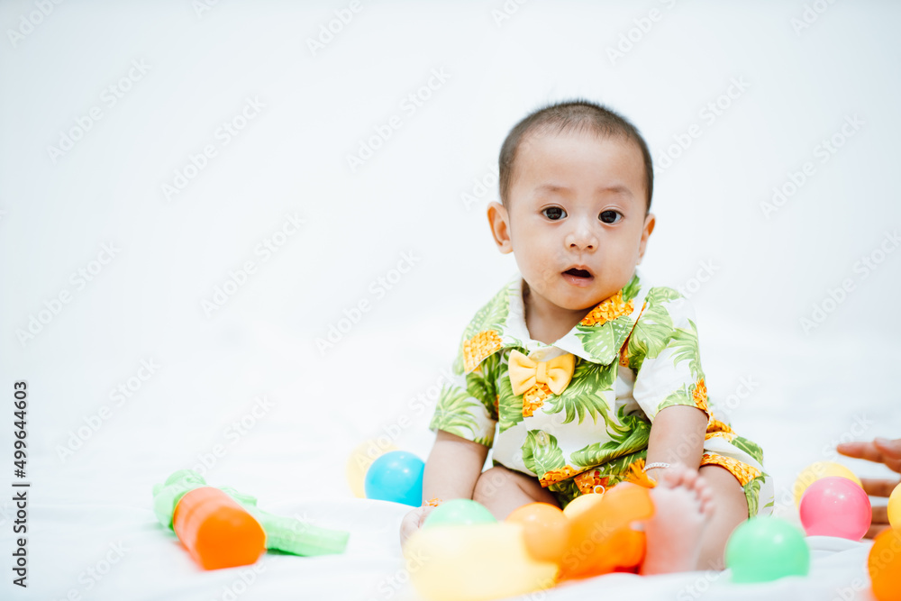 Baby boy wearing a colorful suit is happy and smiles with toys in white room Baby boy wearing a colorful suit is happy and smiles with toys in white room