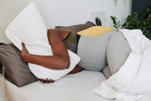 African pregnant woman embracing pillow and suffering from pain lying on bed during childbirth