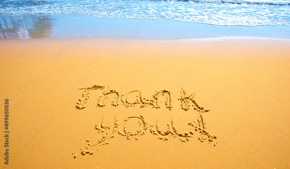 Concept or conceptual hand drawn thank you text carved in a golden sandy beach Concept or conceptual hand drawn thank you text carved in a golden sandy beach