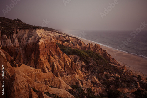 red cliffs drop into moody misty long beach on stormy day in Portugal photo