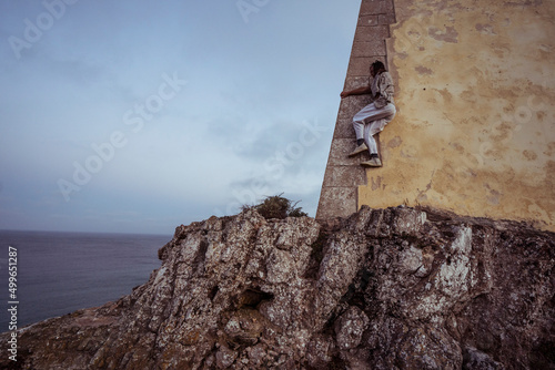 athletic dancer climbs fort wall on ocean cliff in Portugal