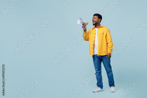 Full body side view young man of African American ethnicity 20s wearig yellow shirt hold scream in megaphone announces discounts sale Hurry up isolated on plain pastel light blue background studio