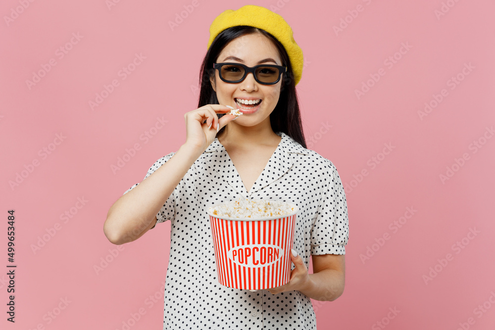 Young smiling happy fun cool woman in 3d glasses watch movie film hold bucket of popcorn look camera isolated on plain pastel background studio portrait. People emotions in cinema lifestyle concept. Young smiling happy fun cool woman in 3d glasses watch movie film hold bucket of popcorn look camera isolated on plain pastel background studio portrait. People emotions in cinema lifestyle concept.
