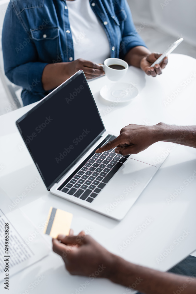 cropped view of senior african american man holding credit card and pointing at laptop. cropped view of senior african american man holding credit card and pointing at laptop.