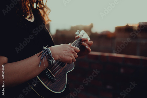 Mujer tocando ukulele en un techo con el atardecer detrás. Concepto de musica.