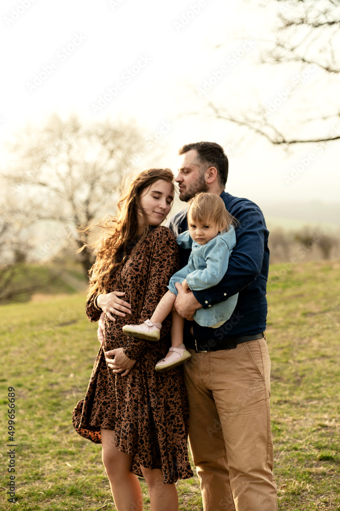 Fototapeta premium a young and happy family walks in nature with their daughter. pregnant woman on a walk with her family. spring walk