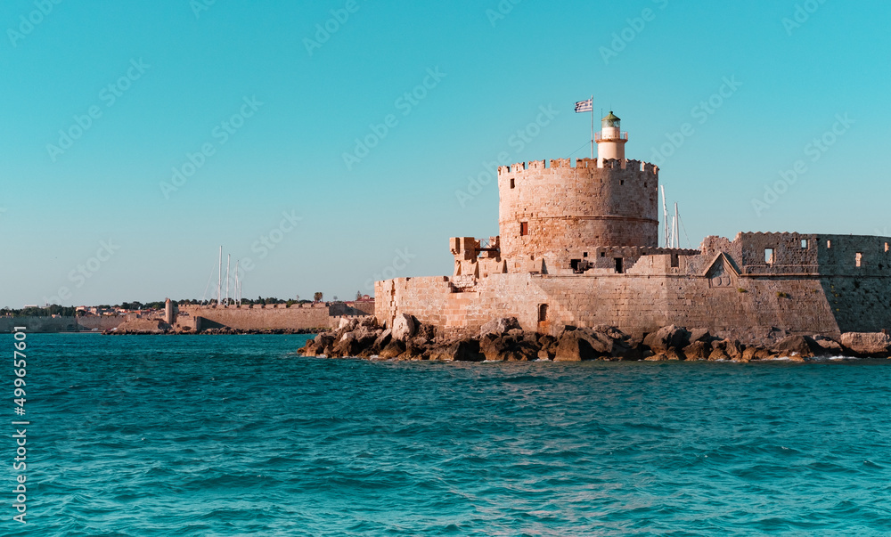 Rhodes Mandraki Port, Rhodes Island, Greece - 05 July 2021: Entrance to Rhodes Old Harbour, Castle fortress of St. Nicolas, Lighthouse, view from sea, former place of Colossus of Rhodes