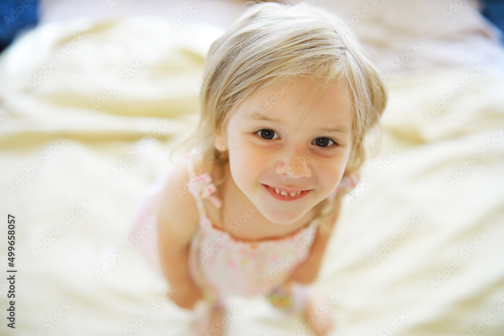 A small child with blond hair lies on the bed. Baby girl is playing on the couch. A small child with blond hair lies on the bed. Baby girl is playing on the couch.