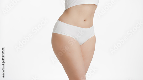 Horizontal medium shot of white-skinned plus size woman's waist and hips in white underwear on white background | Body care concept