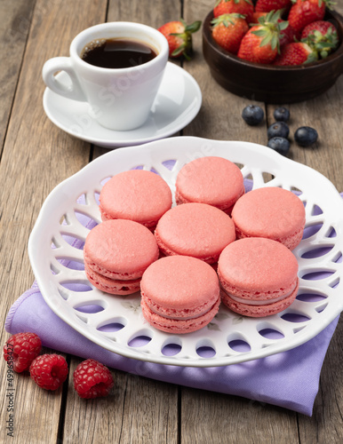 Berry macarons on a plate with coffee over wooden table