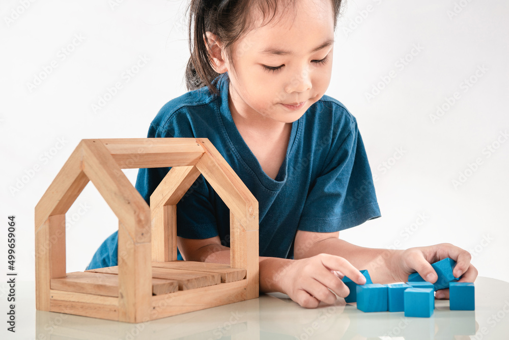 Little girl playing with blue toy blocks and wooden house. A happy kid has concentred to creates constructions with wood bricks. Nursery and childhood educational game for baby and toddler concept Little girl playing with blue toy blocks and wooden house. A happy kid has concentred to creates constructions with wood bricks. Nursery and childhood educational game for baby and toddler concept