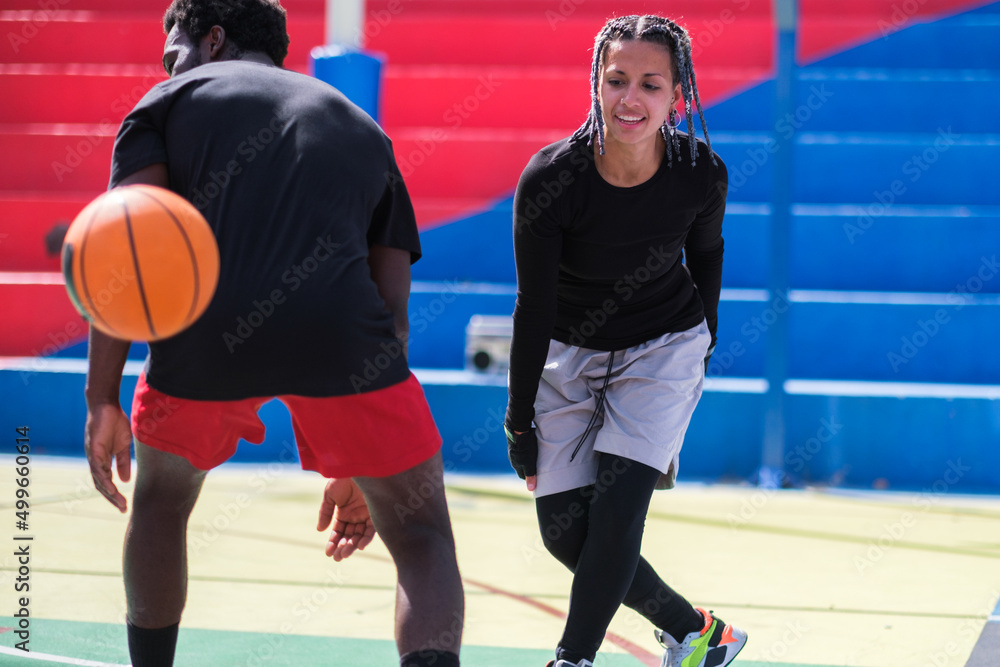 Fototapeta premium Young woman with afro hair playing basketball against men