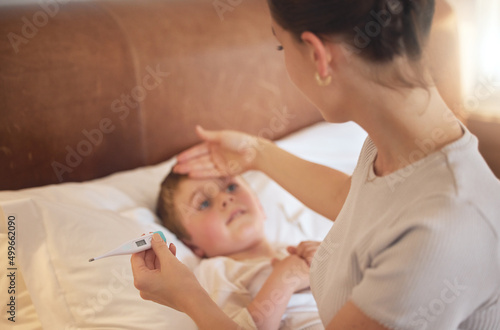 You definitely have a fever. Shot of a woman taking her little boys temperature with a thermometer in bed at home.