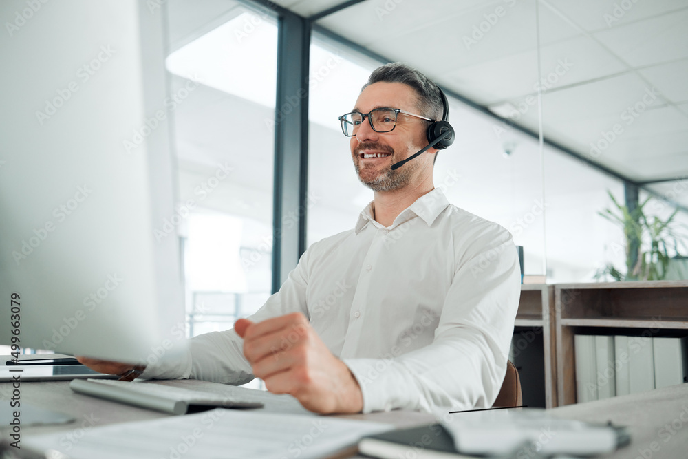 How can I be of service today. Shot of a mature customer service agent sitting alone in the office and using his computer.