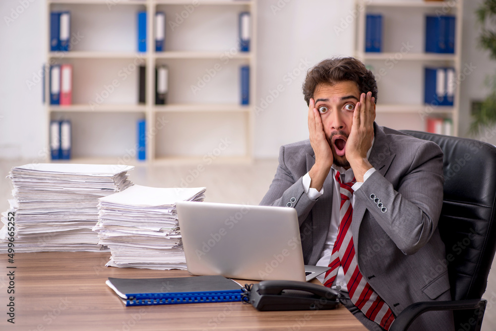 Young male employee unhappy with excessive work in the office Young male employee unhappy with excessive work in the office