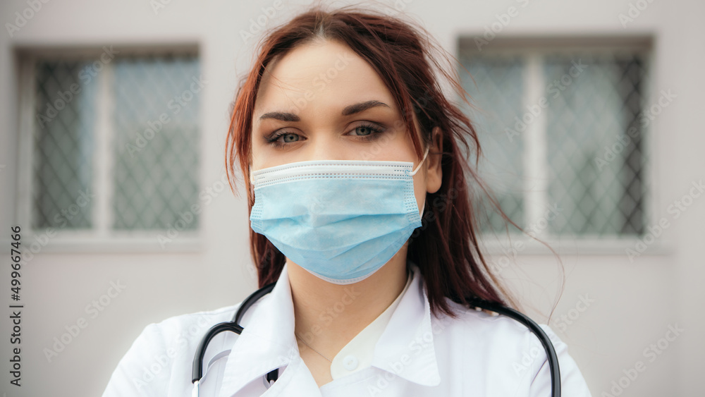 Nurse stand with stethoscope on neck outside street near hospital. Female doctor looking at the camera. Woman wear medical gown, face mask sterilized. Coronavirus healthcare Nurse stand with stethoscope on neck outside street near hospital. Female doctor looking at the camera. Woman wear medical gown, face mask sterilized. Coronavirus healthcare