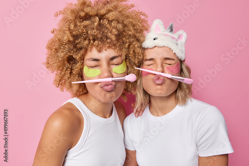Canvas Print Funny women keep eyes closed pouts lips pose with cosmetic brushes for applying makeup apply moisturising beauty patches undergo skin care treatments dressed casually isolated on pink studio wall