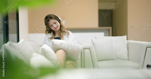 Asian Pretty young woman listening to music from headphones and relaxing while sitting on sofa at home.