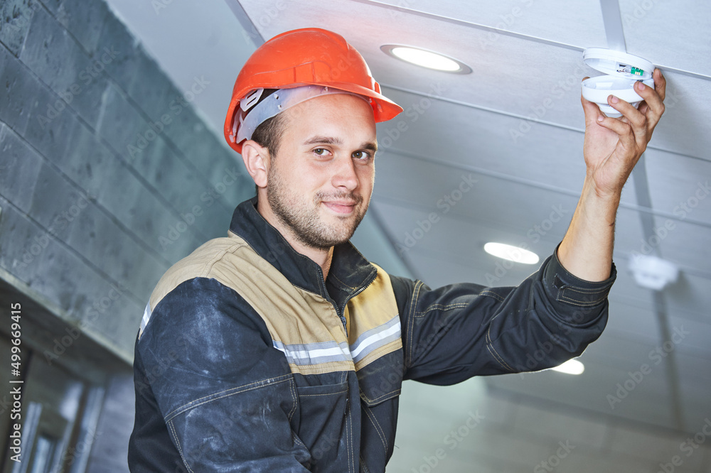 worker installing smoke detector on the ceiling. Fire alarm system installation