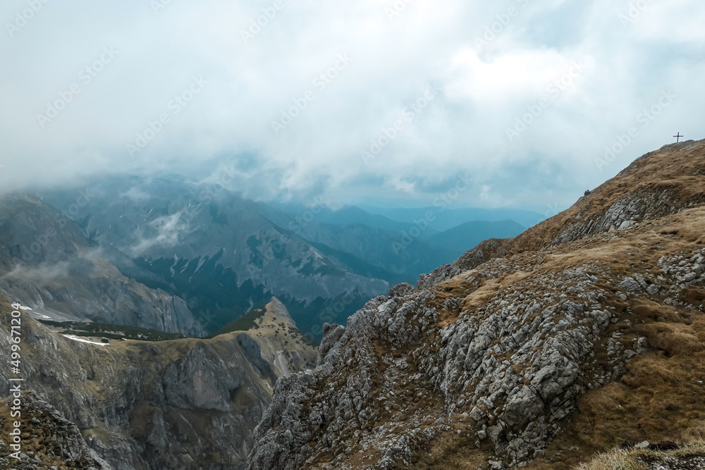 Scenic hiking trail leading to the summit cross of cloud covered mount Zinken in the Hochschwab Region, Upper Styria, Austria. Weather change on rainy spring day in the Alps, Europe. Alpine meadows Scenic hiking trail leading to the summit cross of cloud covered mount Zinken in the Hochschwab Region, Upper Styria, Austria. Weather change on rainy spring day in the Alps, Europe. Alpine meadows
