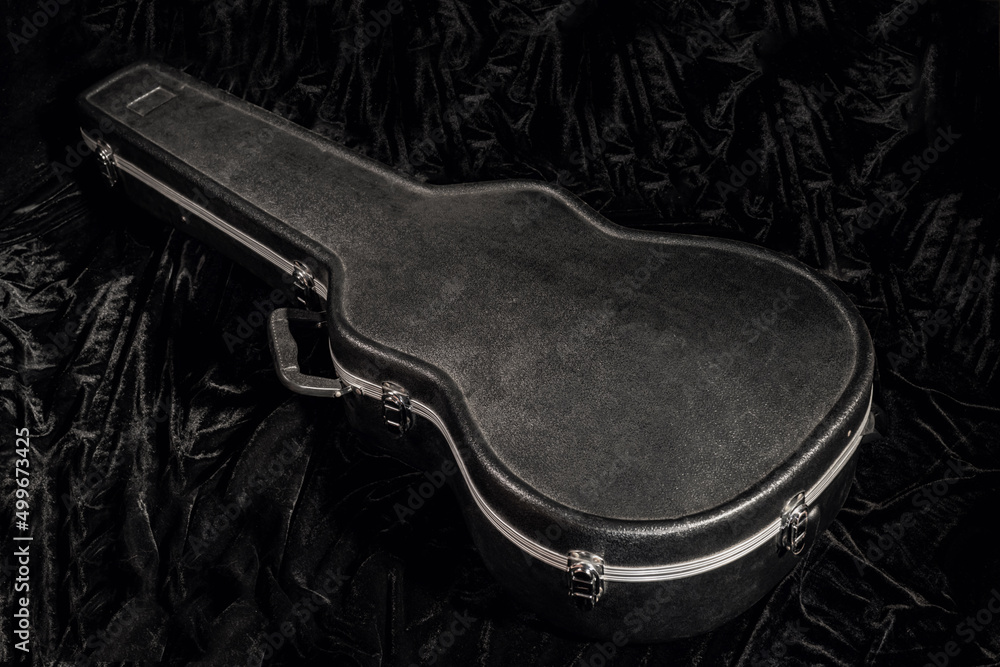 Obraz premium Black hard case for guitar lying on black velor fabric. Closed cover for a stringed musical instrument close up. Black wardrobe trunk for acoustic guitar.