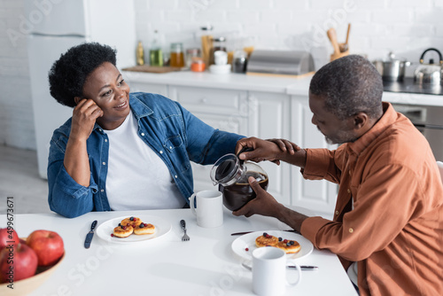 senior african american man pouring coffee to cheerful wife during breakfast.
