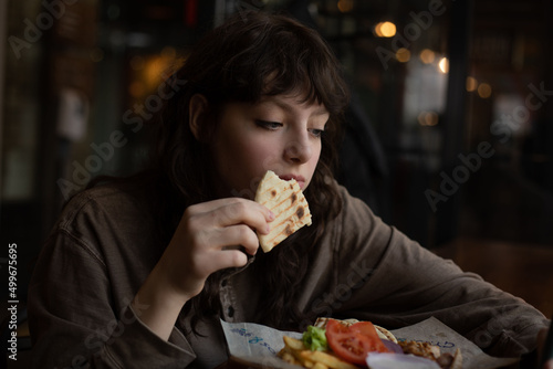 Young woman eating and using phone while sitting in cafe.