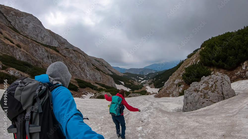 Hiking couple crossing a snow field. Hiking trail in early spring with view on the mountain peaks of Hochschwab Region in Upper Styria, Austria. Snow meadows in Alps, Europe. Man is taking selfies
