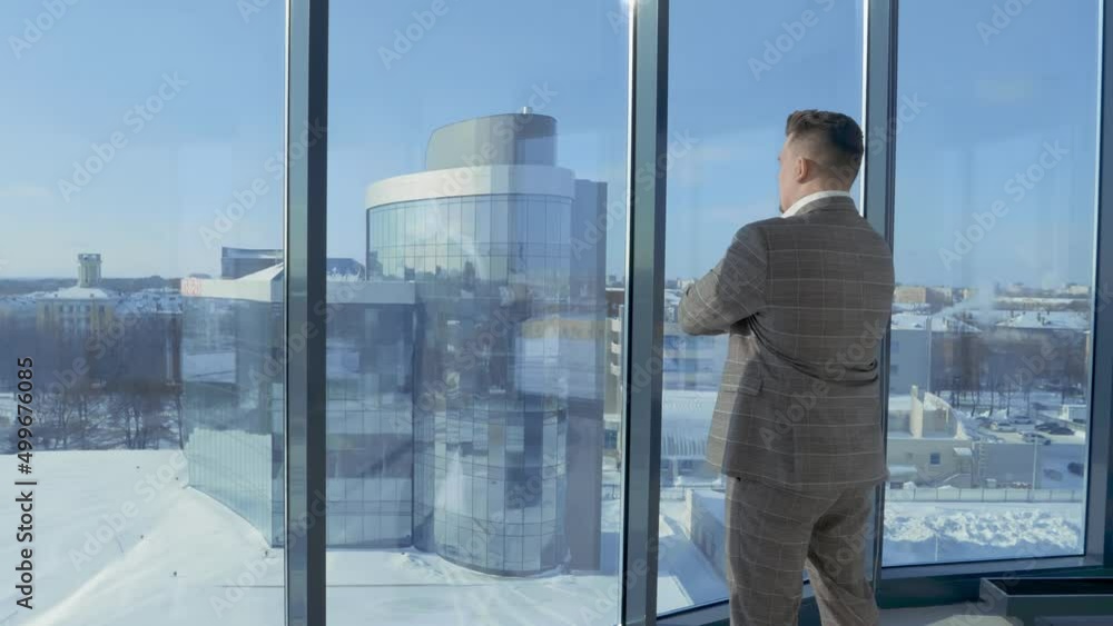Portrait of businessman in suit standing in front of window of office building, enjoying view of business district. Man full of feeling of accomplishment. Concept of result, lifestyle. Portrait of businessman in suit standing in front of window of office building, enjoying view of business district. Man full of feeling of accomplishment. Concept of result, lifestyle.