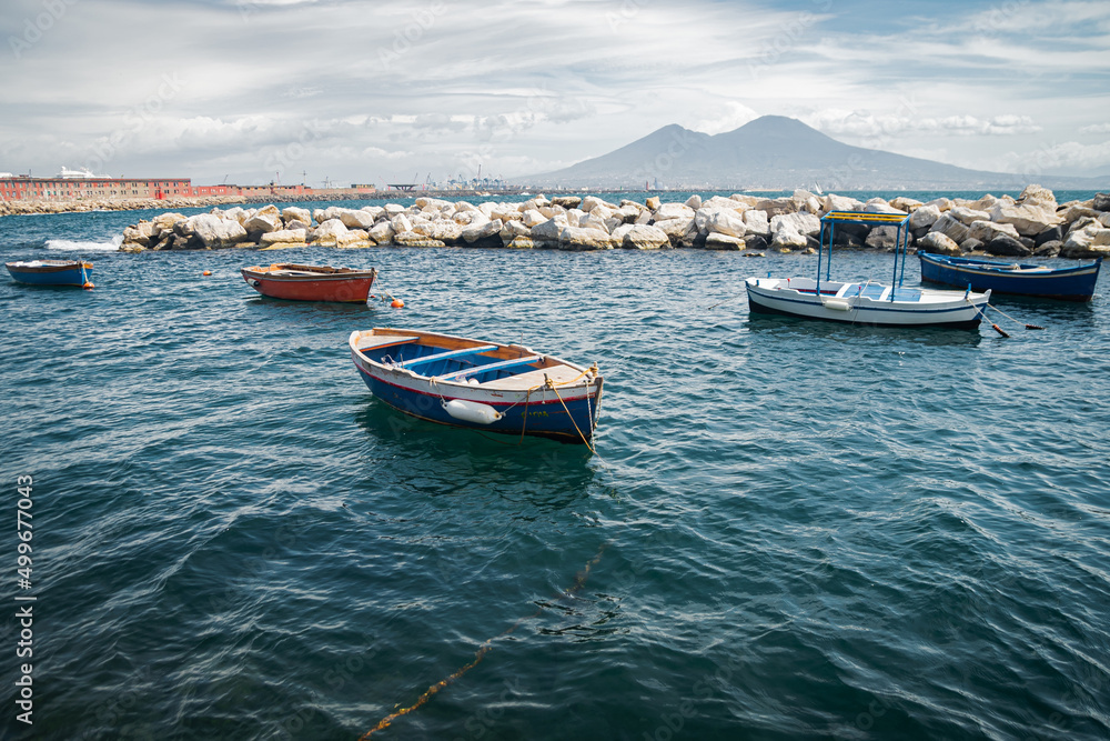 Calm blue Tyrrhenian Sea. View from the embankment of Naples to Mount Vesuvius volcano. Pleasure boats moored near the shore and stone breakwaters.