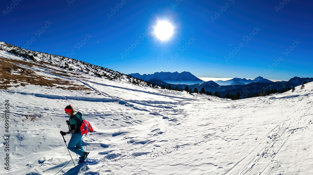 Active woman snow shoe hiking on a trail with scenic view on snow capped mountain peaks of Karawanks in Carinthia, Austria. Ski tour. Julian Alps. Sunny winter day. Freedom. Winter wonderland,Hochobir