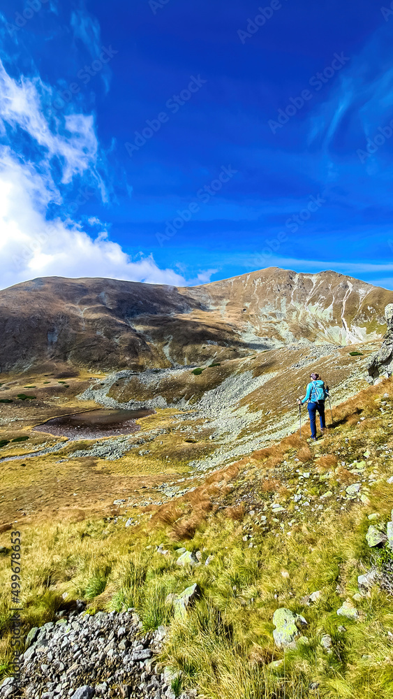 Woman with backpack, view on Haemerkogel in Lower Tauern mountain range, Styria, Austria, Europe. Sunny golden autumn day in Seckau Alps. Scenic hiking trail to Seckauer Zinken on dry, bare terrain
