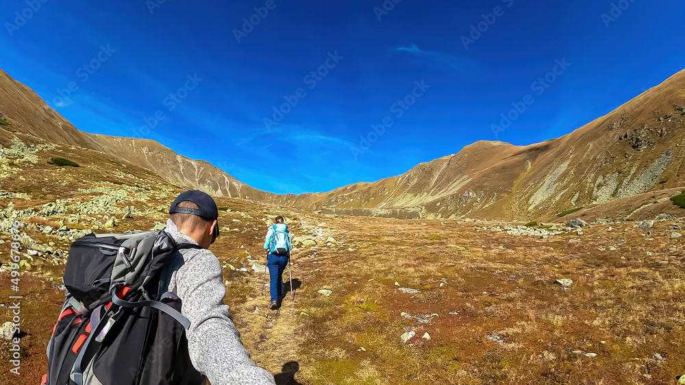 Couple with backpack on hiking trail leading to Seckauer Zinken in the Lower Tauern mountain range, Styria, Austria, Europe. Sunny golden autumn day in Seckau Alps. Panorama on dry, bare grass terrain