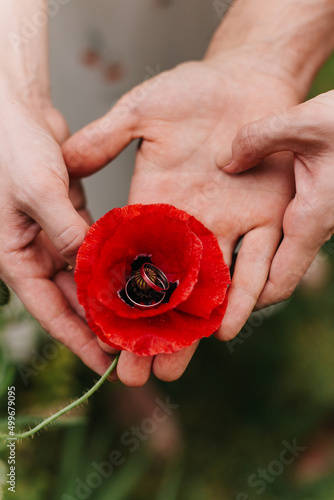 young couple holding a red poppy flower in the heart of which are engagement rings