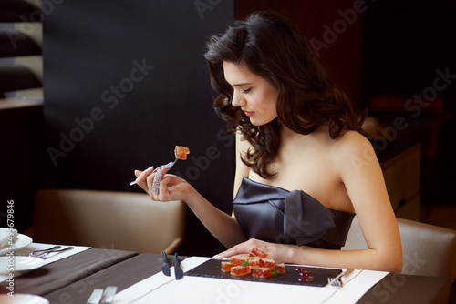 Young woman in elegant dress with bare shoulders, serves a dessert in the restaurant, with makeup and hairstyle.