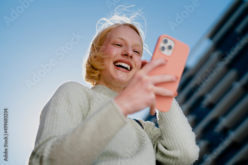 Happy girl walking on the street checking phone. Beautiful blonde girl typing a message..