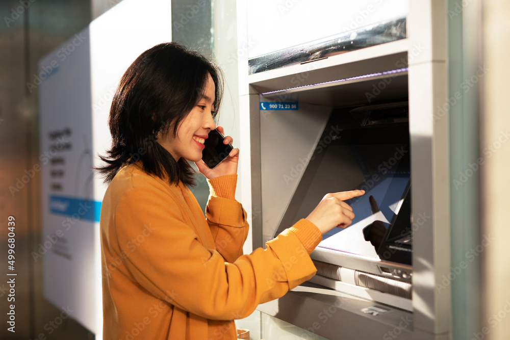 Happy smiling young woman withdrawing money from credit card. Young woman typing pin code on keypad of ATM machine Happy smiling young woman withdrawing money from credit card. Young woman typing pin code on keypad of ATM machine