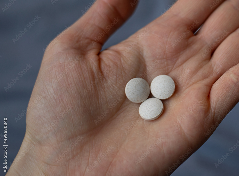 A woman holding three white round pills in her hand A woman holding three white round pills in her hand
