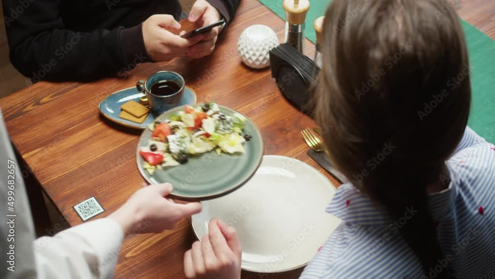 Scanning QR code in restaurant. Woman eating salad, using qr code with smartphone, online menu in cafe. Modern technology, ordering meal in application. Contactless touch-free payment in app.