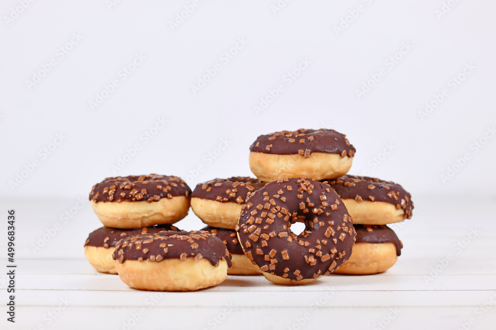 Donuts glazed with chocolate and with sprinkles on white wooden background with copy space